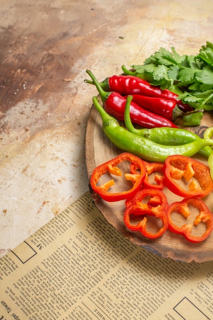 Vista de la mitad inferior diferentes verduras cilantro pimientos picantes pimientos cortados en trozos en un tablero de madera de árbol redondo un periódico sobre fondo ámbar espacio libre