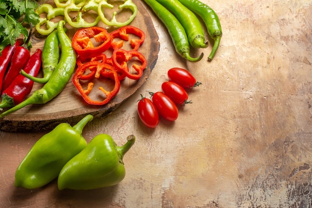 Vista de la mitad inferior diferentes verduras cilantro pimientos picantes pimientos cortados en trozos en un tablero de madera de árbol redondo tomates cherry pimientos sobre fondo amarillo ocre espacio libre