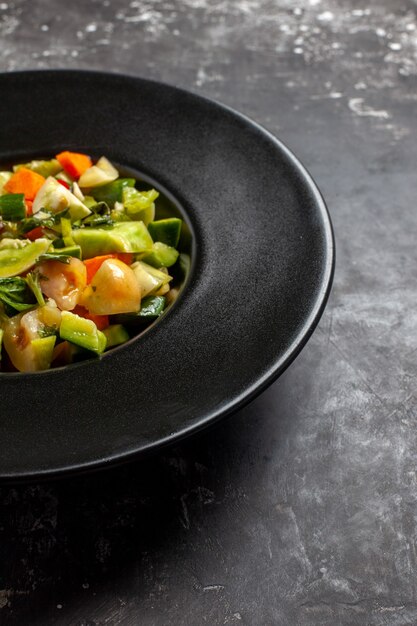 Vista de la mitad inferior ensalada de tomate verde en placa ovalada sobre fondo oscuro