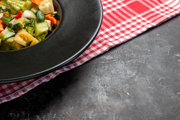 Vista de la mitad inferior ensalada de tomate verde en placa ovalada un tenedor sobre fondo oscuro