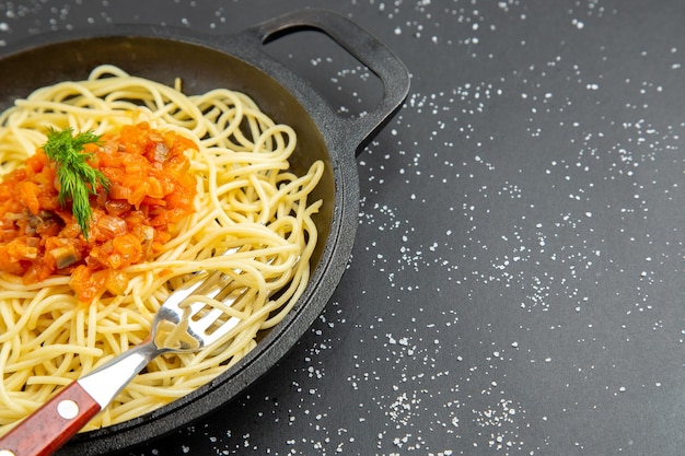Vista de la mitad inferior de espaguetis con salsa en una sartén en el cuadro negro