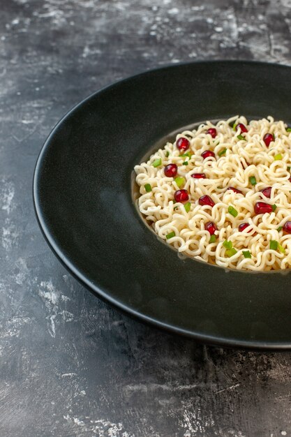 Vista de la mitad inferior de fideos ramen asiáticos en plato redondo negro sobre mesa oscura