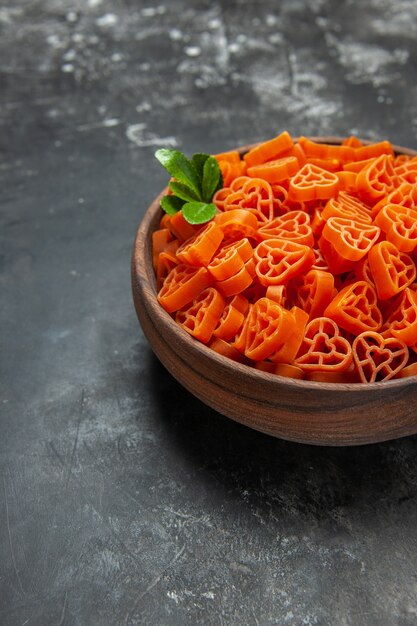 Vista de la mitad inferior de pasta italiana roja en forma de corazón en un recipiente sobre una superficie oscura