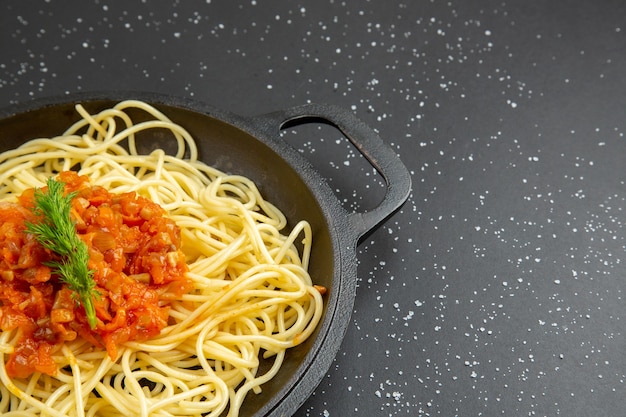 Vista de la mitad inferior sabrosos espaguetis en una sartén en el cuadro negro