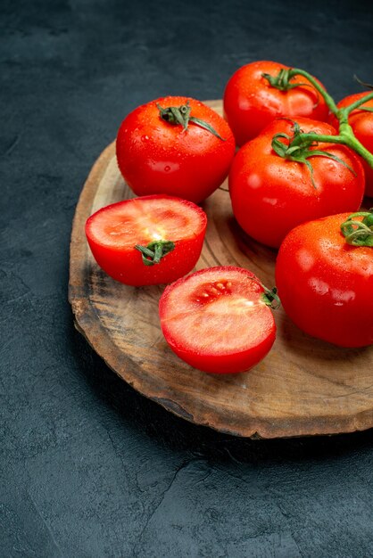 Vista de la mitad inferior del tablero de madera de tomates rojos frescos en la mesa oscura