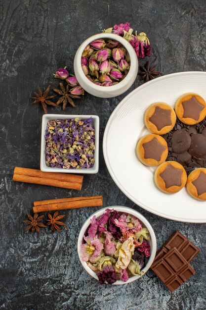 Vista de la mitad izquierda de un plato de galletas con flores secas y canela y chocolates sobre suelo gris