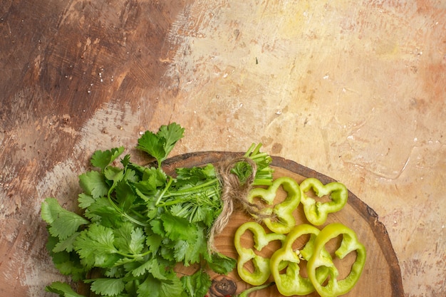 Foto gratuita vista de la mitad superior de diferentes verduras cilantro pimientos cortados en trozos en la tabla de madera de árbol redondo sobre fondo ámbar