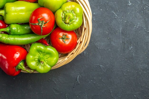 Foto gratuita vista de la mitad superior de pimientos y tomates en un tazón de canasta de mimbre sobre fondo oscuro con espacio libre