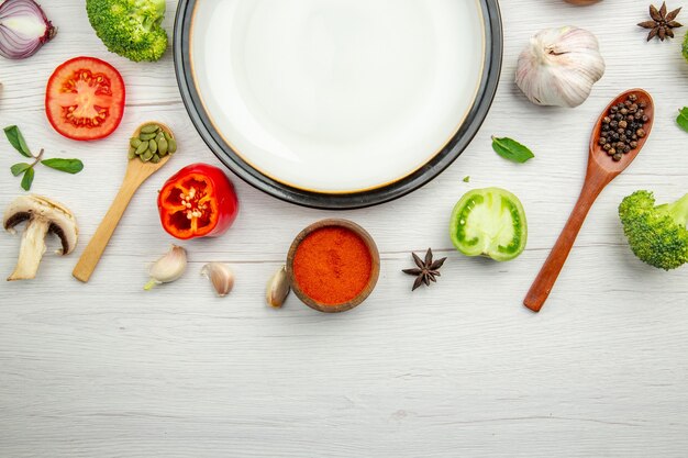 Vista de la mitad superior plato blanco tomate verde pimiento rojo en polvo en un tazón de pimienta negra en cuchara de madera anís ajo en mesa gris