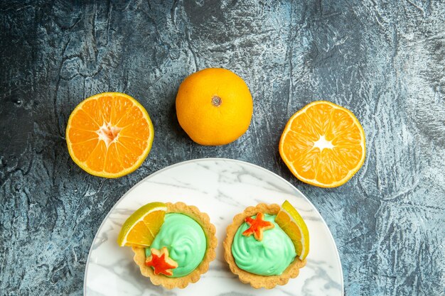 Vista de la mitad superior tartas pequeñas con crema pastelera verde y una rodaja de limón en un plato cortadas naranjas sobre una superficie oscura