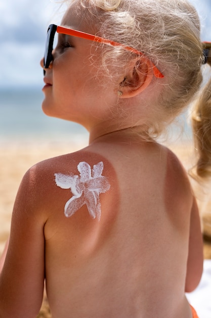 Foto gratuita vista de niña en la playa con loción en la piel quemada por el sol