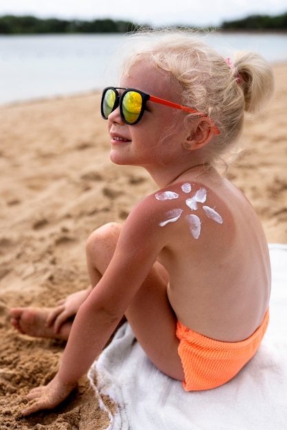 Foto gratuita vista de niña en la playa con loción en la piel quemada por el sol