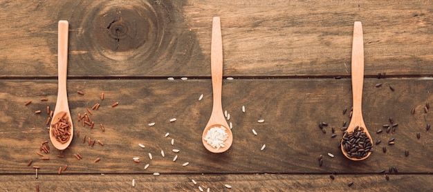 Vista panorámica de la cuchara de madera con arroz blanco y marrón en la mesa de madera