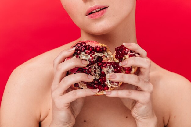 Vista parcial de chica sensual con granada. Foto de estudio de mujer con jugoso granate aislado sobre fondo rojo.