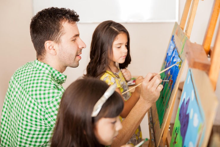 Foto gratuito vista de perfil de un apuesto profesor de arte trabajando en una pintura con uno de sus alumnos en clase