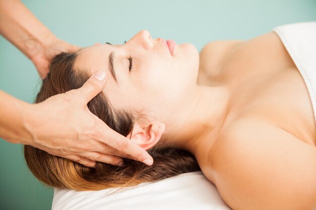 Vista de perfil de una hermosa joven que recibe un masaje en la cabeza por parte de un terapeuta en una clínica de belleza y spa