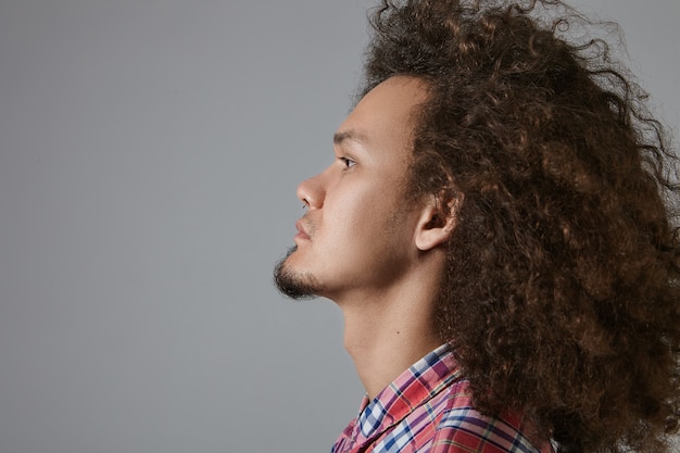 Vista de perfil de hombre barbudo de raza mixta joven serio elegante con peinado rizado vestido con camisa a cuadros