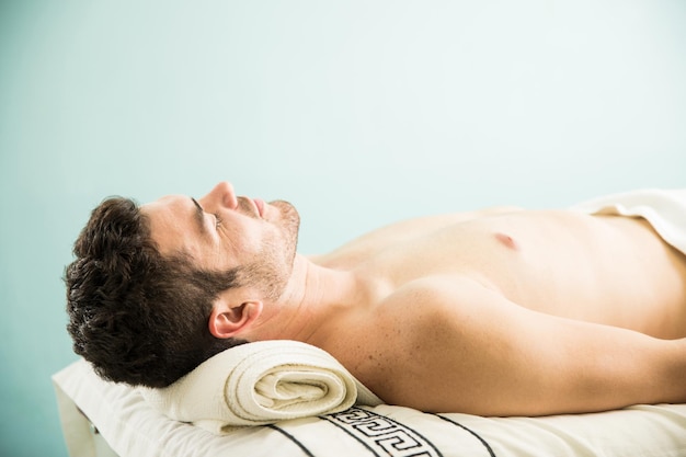 Vista de perfil de un joven acostado en una cama y tomando una siesta después de un masaje en un spa