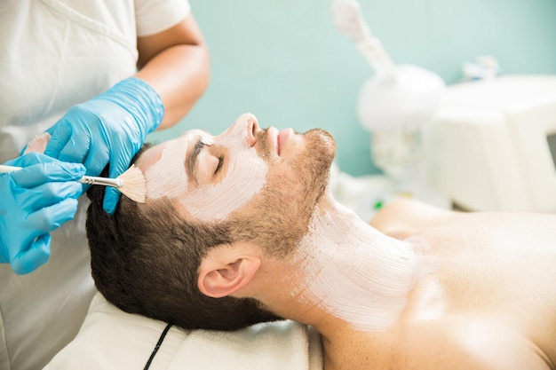 Vista de perfil de un joven que recibe un tratamiento facial hidratante en un spa de salud