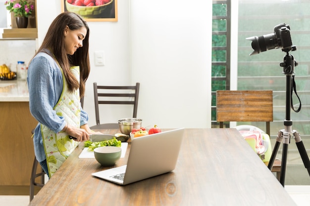 Vista de perfil de una mujer joven que se graba a sí misma cocinando un plato para su blog de video