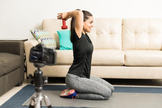 Vista de perfil de una mujer joven con ropa deportiva grabando un video para su blog de fitness