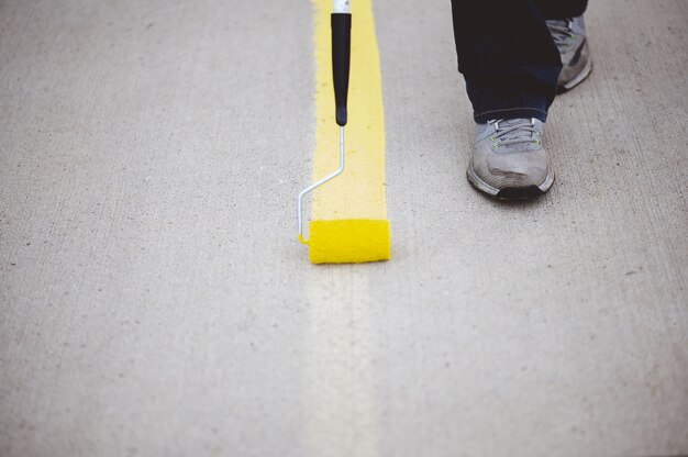 Vista de una persona repintando las líneas de estacionamiento del asfalto de un estacionamiento con pintura amarilla