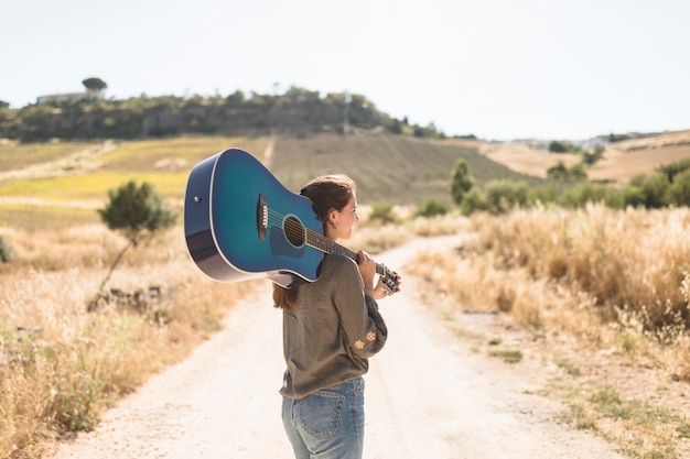 Vista posterior de una adolescente de pie en el camino de tierra con guitarra