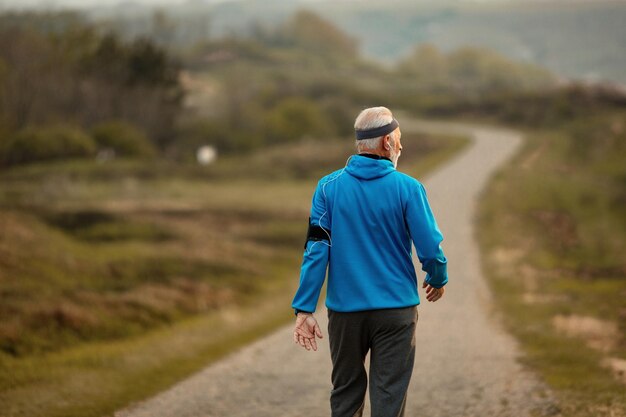 Vista posterior del atleta senior caminando por la carretera en la naturaleza mientras mantiene su estilo de vida saludable Copiar espacio