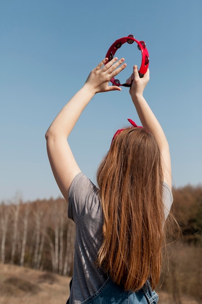 Vista posterior de despreocupada mujer tocando la pandereta en la naturaleza