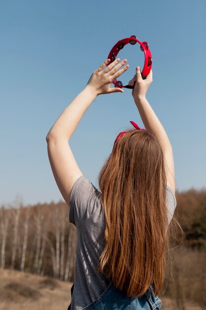 Vista posterior de despreocupada mujer tocando la pandereta en la naturaleza