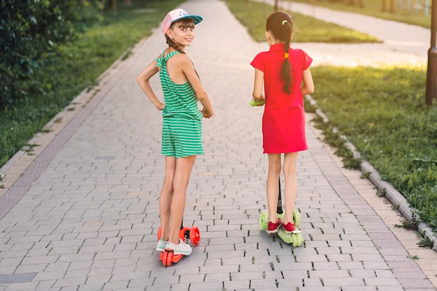 Foto gratuita vista posterior de dos niñas montando scooter en el parque