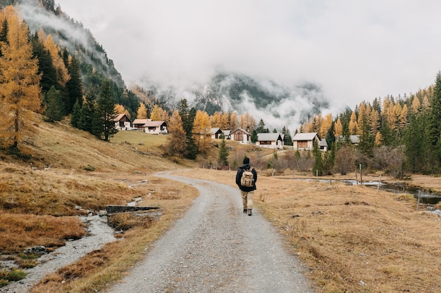 Vista posterior de un excursionista hombre con una mochila caminando por un sendero rodeado de escenas de la naturaleza otoñal