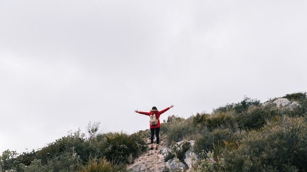 Vista posterior de un excursionista de pie en la cima de la montaña estirándose las manos