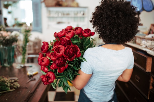 Foto gratuita vista posterior de una floristería femenina africana con ramo de flores rojas