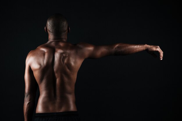 Vista posterior de la foto de un hombre deportista musculoso semidesnudo, con la mano derecha hacia arriba