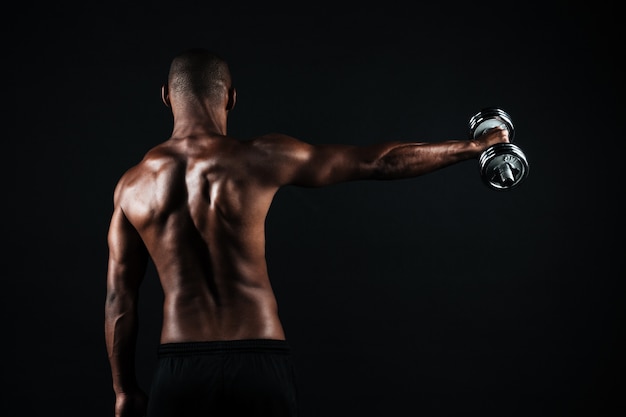 Vista posterior de la foto de un hombre deportista musculoso semidesnudo, con pesas en la mano derecha