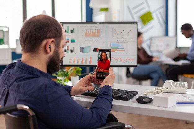 Vista posterior del gerente de proyecto con teléfono inteligente escuchando a la compañía líder remota en una videollamada, hablando en línea con auriculares, discutiendo en una reunión virtual sobre el proyecto financiero