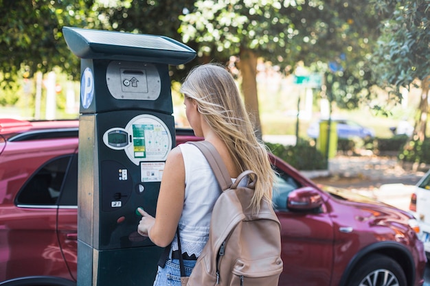 Vista posterior de la hembra joven que paga estacionamiento en la calle