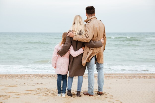 Vista posterior de una hermosa familia con una pequeña hija divirtiéndose en la playa juntos