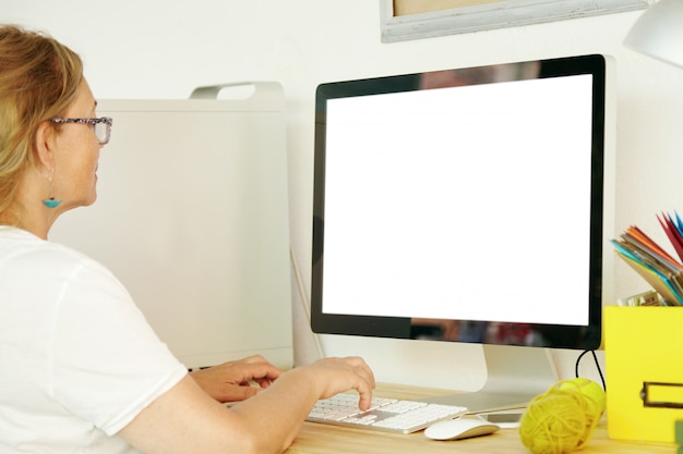 Vista posterior de una hermosa mujer madura con una camiseta blanca usando una PC con una pantalla de espacio de copia en blanco para su texto promocional o contenido publicitario, pagando facturas domésticas en línea, revisando el correo electrónico