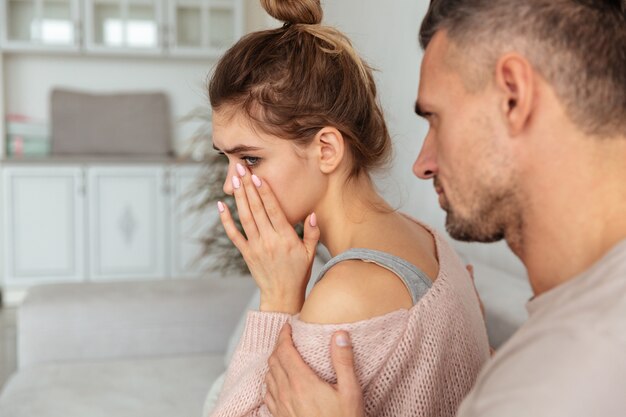 Vista posterior del hombre cuidadoso sentado en el sofá y calmar a su novia molesta que llora en casa