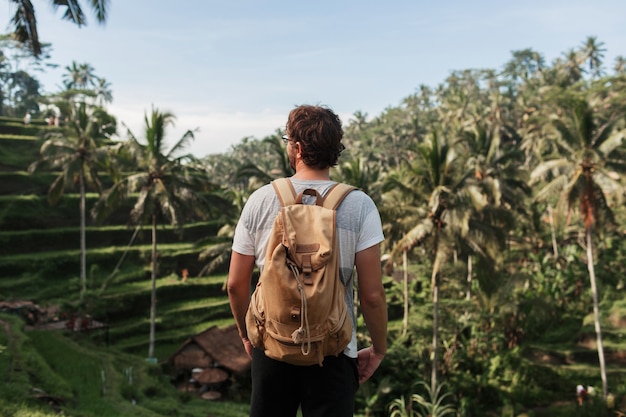 Vista posterior del hombre explorador con mochila de viaje disfrutando del entorno natural de la plantación green rise durante el viaje en Bali