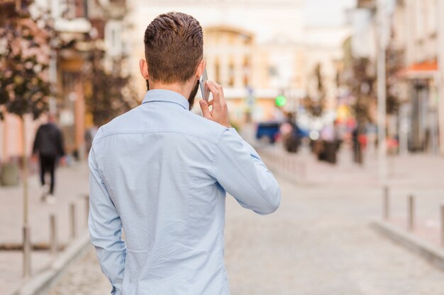Vista posterior de un hombre hablando por teléfono inteligente al aire libre