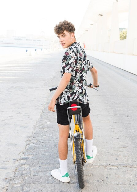 Vista posterior de un hombre joven con bicicleta mirando a cámara