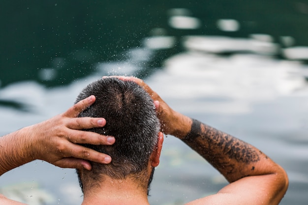 Vista posterior de un hombre lavándose el cabello frente al lago