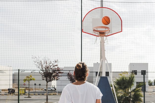 Vista posterior de un hombre mirando baloncesto pasando por un aro en la corte