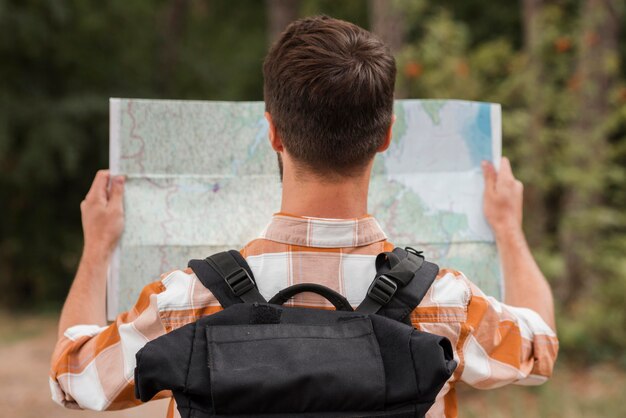 Vista posterior del hombre con mochila mirando el mapa mientras acampa