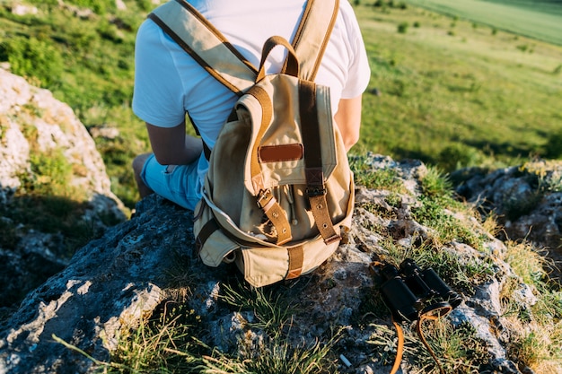 Vista posterior de un hombre con mochila sentado en la roca