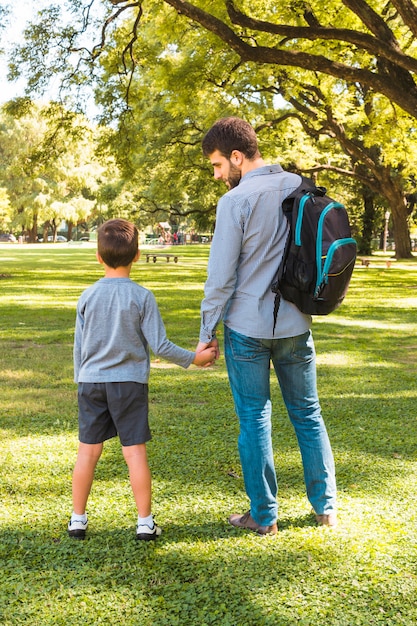 Vista posterior de un hombre de pie con su hijo en el parque