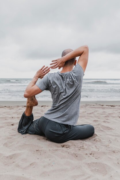 Vista posterior del hombre en la playa haciendo yoga